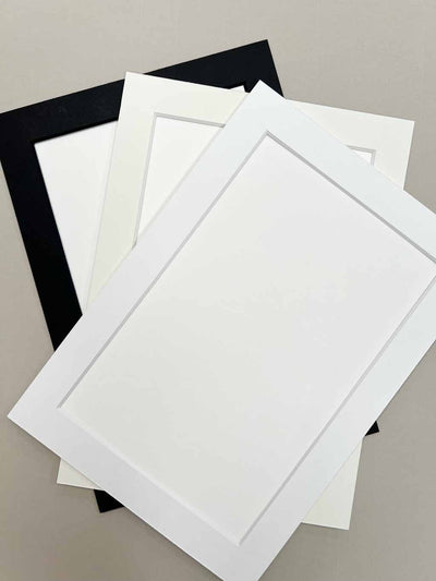 Assorted custom window mount frames displayed in black, white, and clear, lying on a surface.